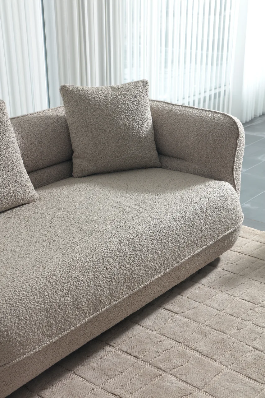 Light-coloured sofa with a textured surface, curved arm and seam along the seat edge